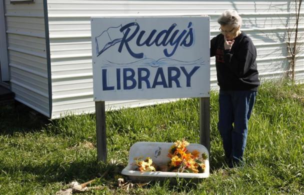 Elsie Eiler poses with the sign outside the 5,000 book library in the village of Monowi